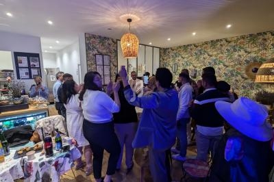Groupe de personnes debout dans une pièce décorée, discutant et partageant un moment convivial autour de tables dressées.