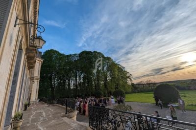 Groupe de personnes rassemblées sur une terrasse devant un bâtiment historique, avec un jardin et un coucher de soleil en…