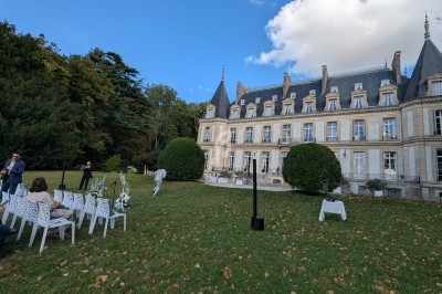 Façade d'un château entouré de verdure avec des chaises blanches disposées pour un événement en plein air.