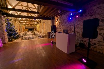 Salle de réception en pierre avec éclairage tamisé, piste de danse, tables dressées et équipement de DJ installé.