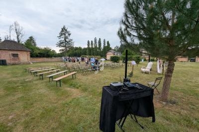 Installation d'un espace extérieur pour un événement avec bancs alignés, table de mixage et arbres en arrière-plan.