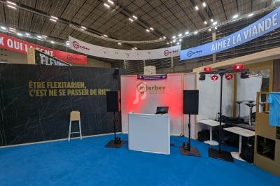 Stand d'exposition avec une table, des enceintes et un panneau affichant le message ’Être flexitarien, c'est ne se passer de…