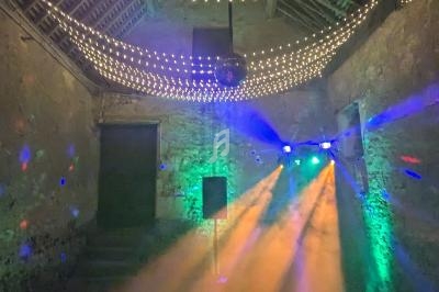 Salle en pierre avec plafond en bois, éclairée par des guirlandes lumineuses et des projecteurs colorés.