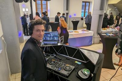 Un DJ anime un événement dans une salle avec des invités debout près de tables de buffet.