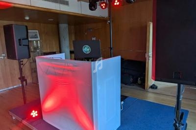 Un stand de DJ avec platine, éclairage rouge et enceintes, installé sur une petite scène dans une salle en bois.