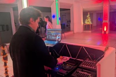 Un DJ mixe sur une console dans une salle éclairée de lumières colorées, avec un sapin de Noël en arrière-plan.