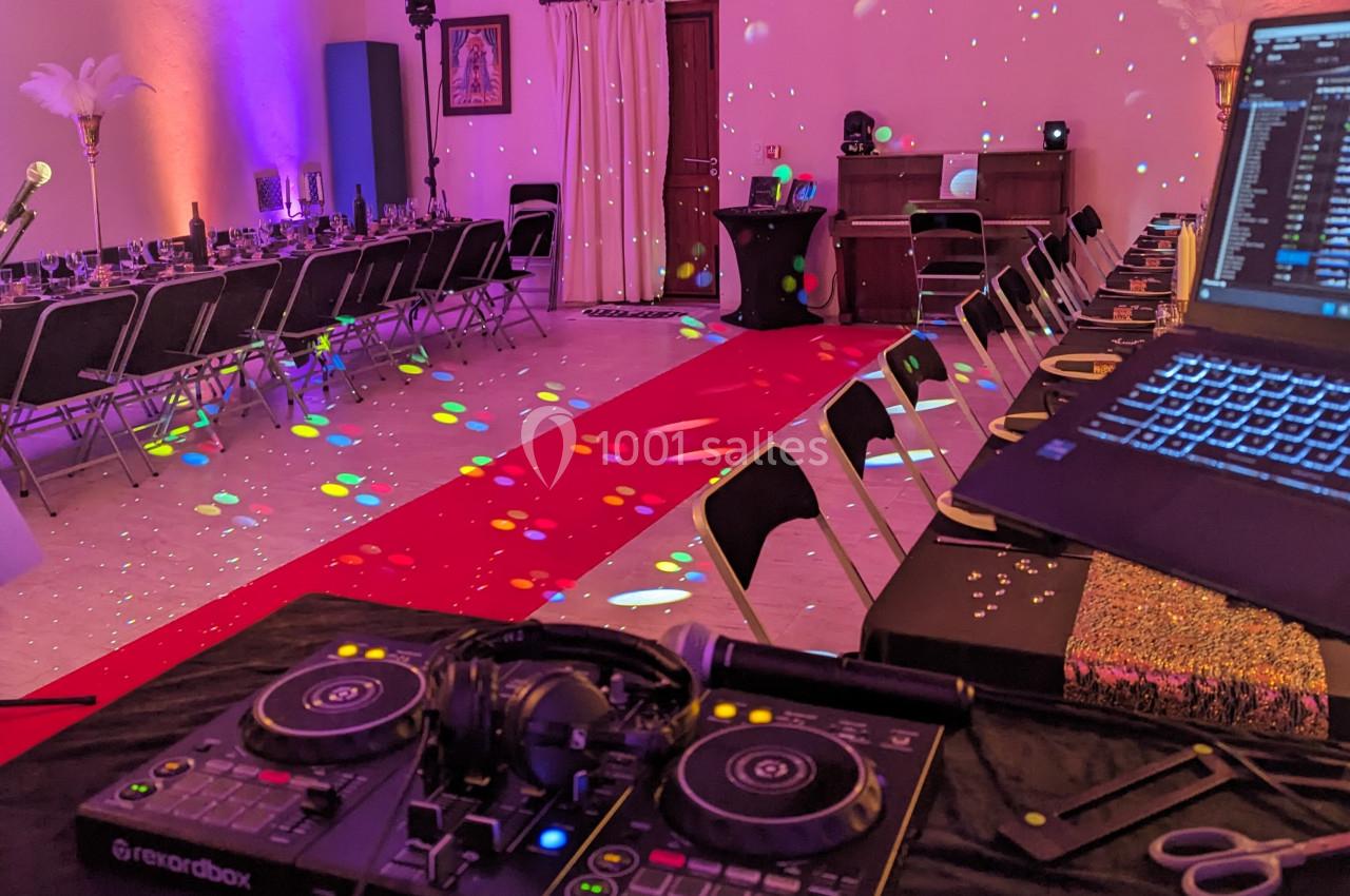 Salle décorée pour un événement avec tables alignées, piste rouge centrale et matériel de DJ au premier plan.