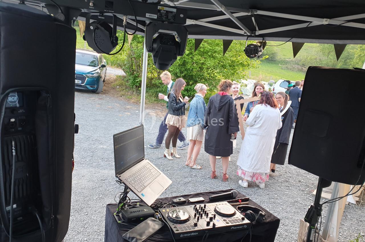 Vue depuis une table de DJ avec platines et ordinateur, face à un groupe de personnes discutant en extérieur.
