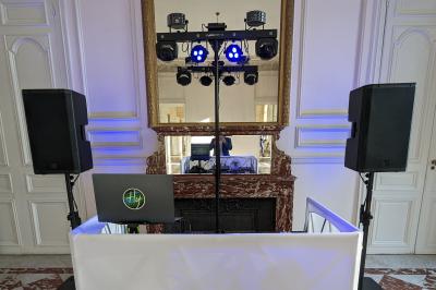 Un homme s'exprime au micro devant un public rassemblé dans une cour extérieure entourée de végétation.