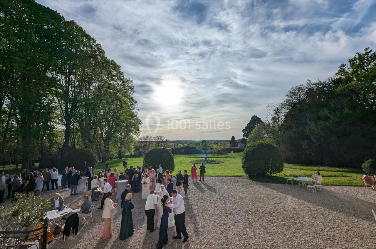 Groupe de personnes rassemblées dans une cour extérieure avec vue sur un jardin et un ciel partiellement nuageux.
