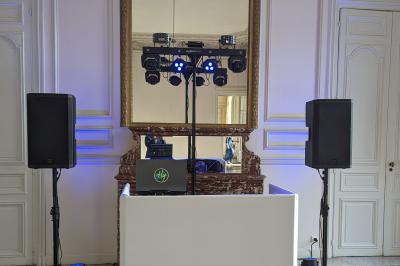 Un homme s'exprime au micro devant un public rassemblé dans une cour extérieure entourée de végétation.