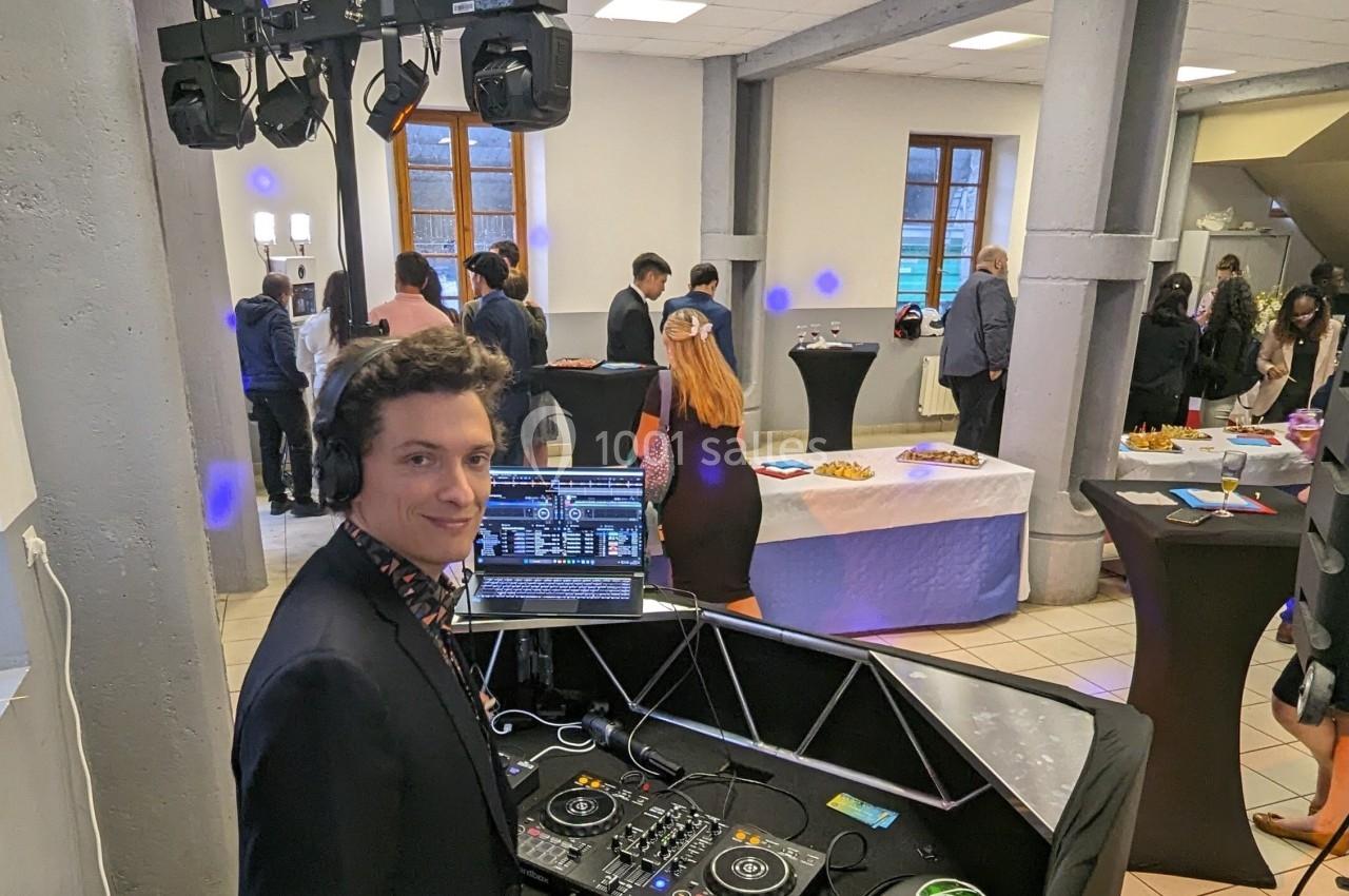 Un DJ anime une réception dans une salle avec des invités debout autour de tables hautes.