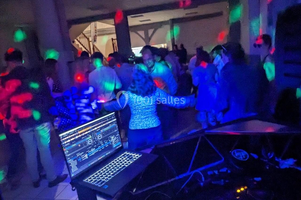 Personnes dansant dans une salle sombre éclairée par des lumières colorées, avec un ordinateur de DJ au premier plan.