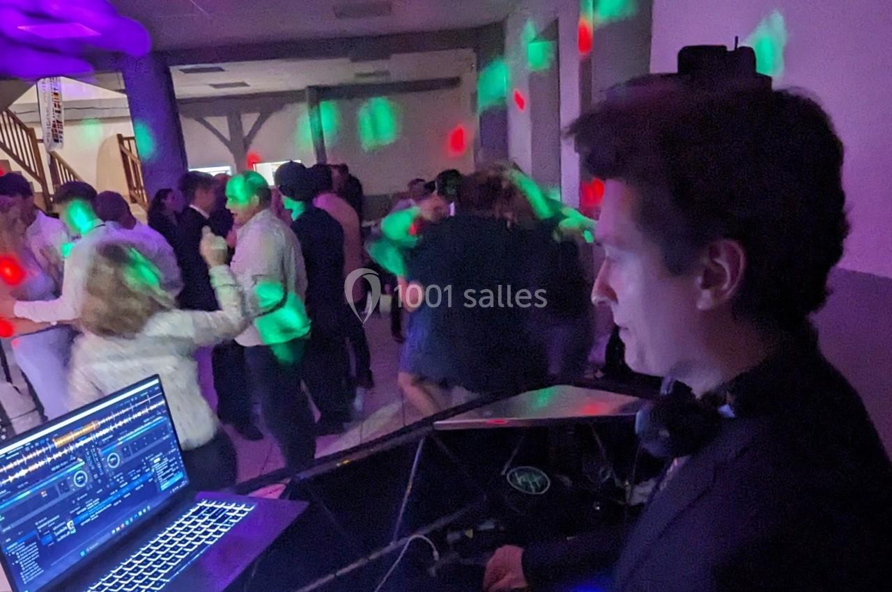 Un DJ mixe de la musique lors d'une soirée dansante avec des invités sur une piste éclairée par des lumières colorées.