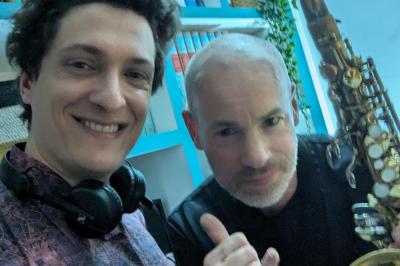 Un homme s'exprime au micro devant un public rassemblé dans une cour extérieure entourée de végétation.