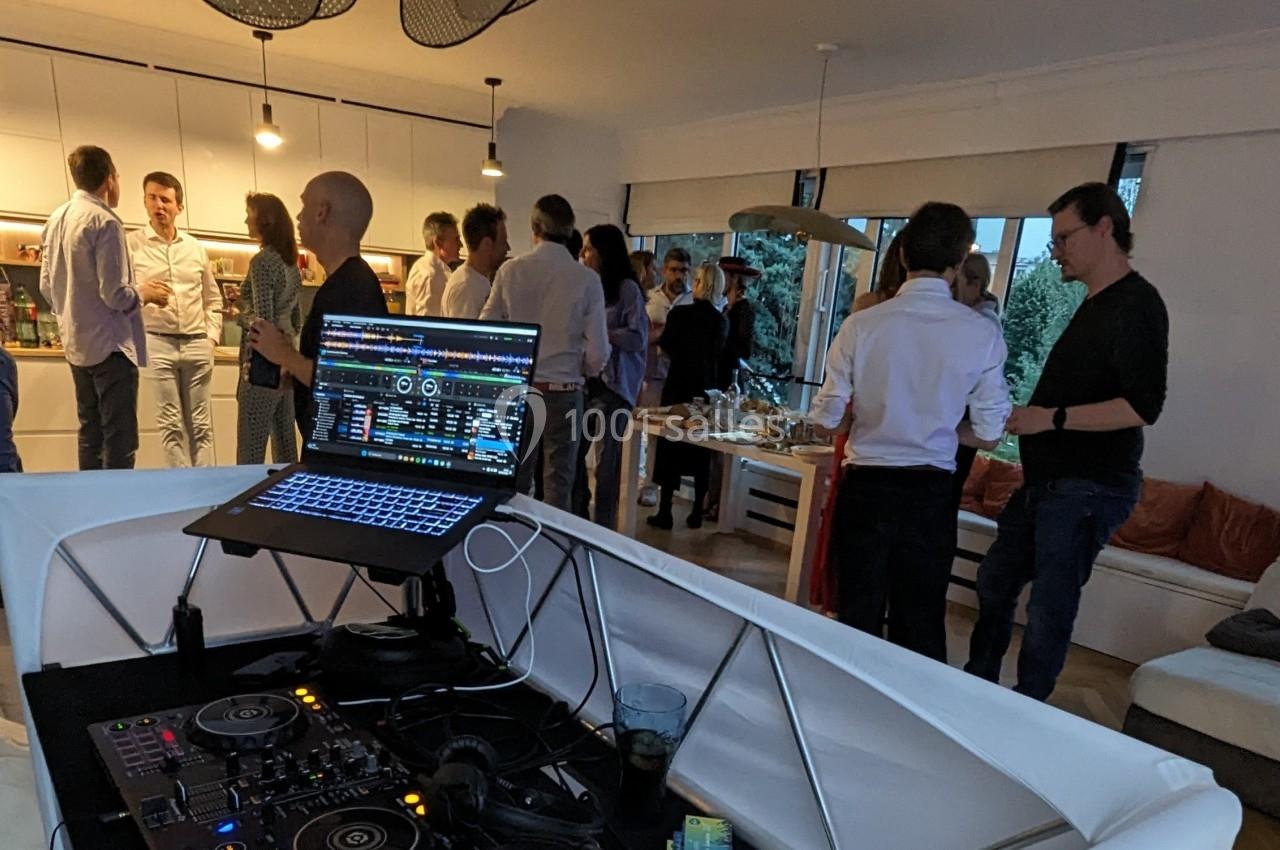 Vue d'une soirée conviviale avec des invités discutant dans un salon, un équipement de DJ visible au premier plan.