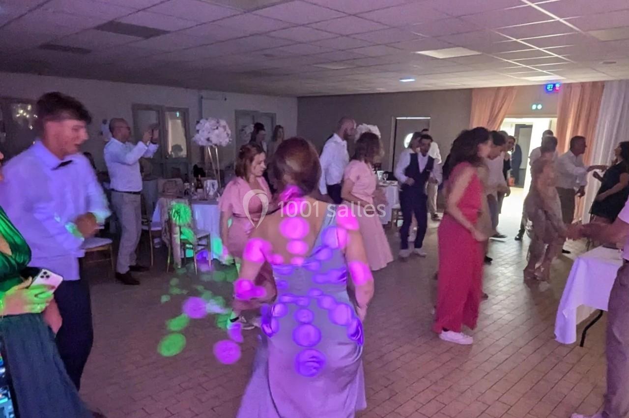 Des personnes dansent dans une salle éclairée par des lumières colorées, lors d'un événement festif.