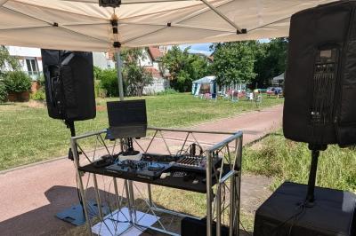 Un homme s'exprime au micro devant un public rassemblé dans une cour extérieure entourée de végétation.