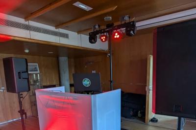 Un homme s'exprime au micro devant un public rassemblé dans une cour extérieure entourée de végétation.