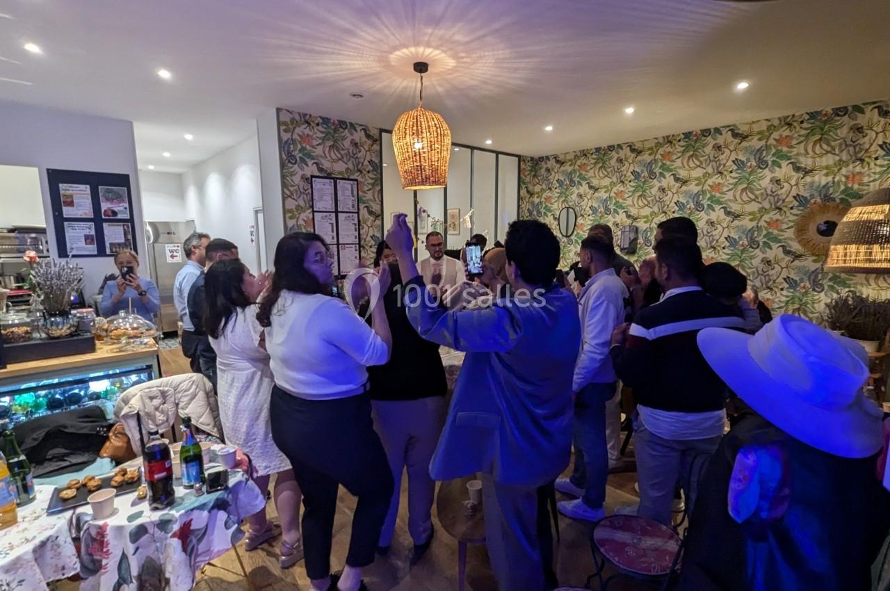 Groupe de personnes debout dans une pièce décorée, discutant et célébrant autour de tables avec des boissons et des snacks.