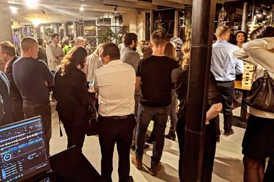 Un homme s'exprime au micro devant un public rassemblé dans une cour extérieure entourée de végétation.