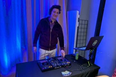 Un homme s'exprime au micro devant un public rassemblé dans une cour extérieure entourée de végétation.