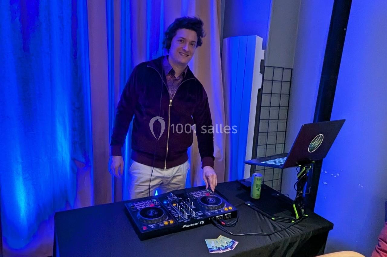 Un homme souriant utilise une table de mixage DJ sur une table, entouré d'un éclairage bleu.