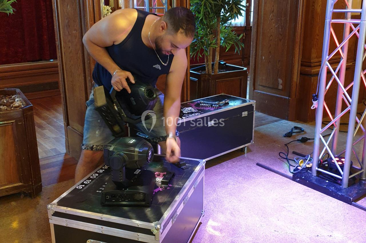 Un technicien ajuste un projecteur sur une caisse de matériel dans une salle avec des structures lumineuses.