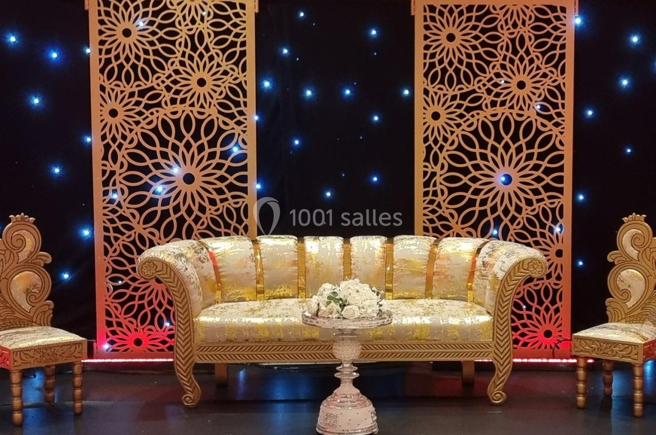 Canapé doré et deux fauteuils assortis devant des panneaux décoratifs ajourés, éclairés par des lumières scintillantes.