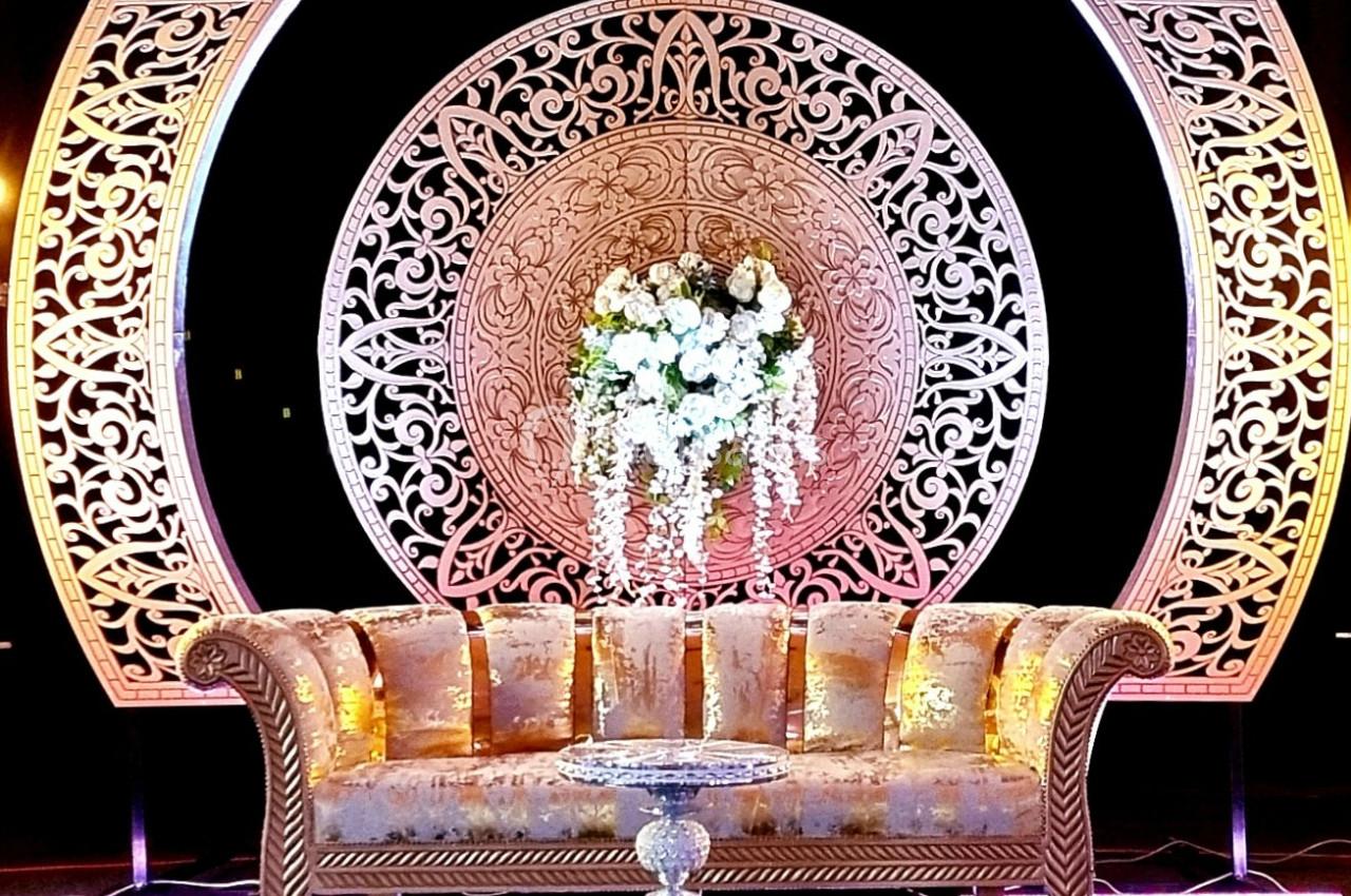 Canapé doré devant une décoration circulaire ornée de motifs complexes et de fleurs blanches suspendues.