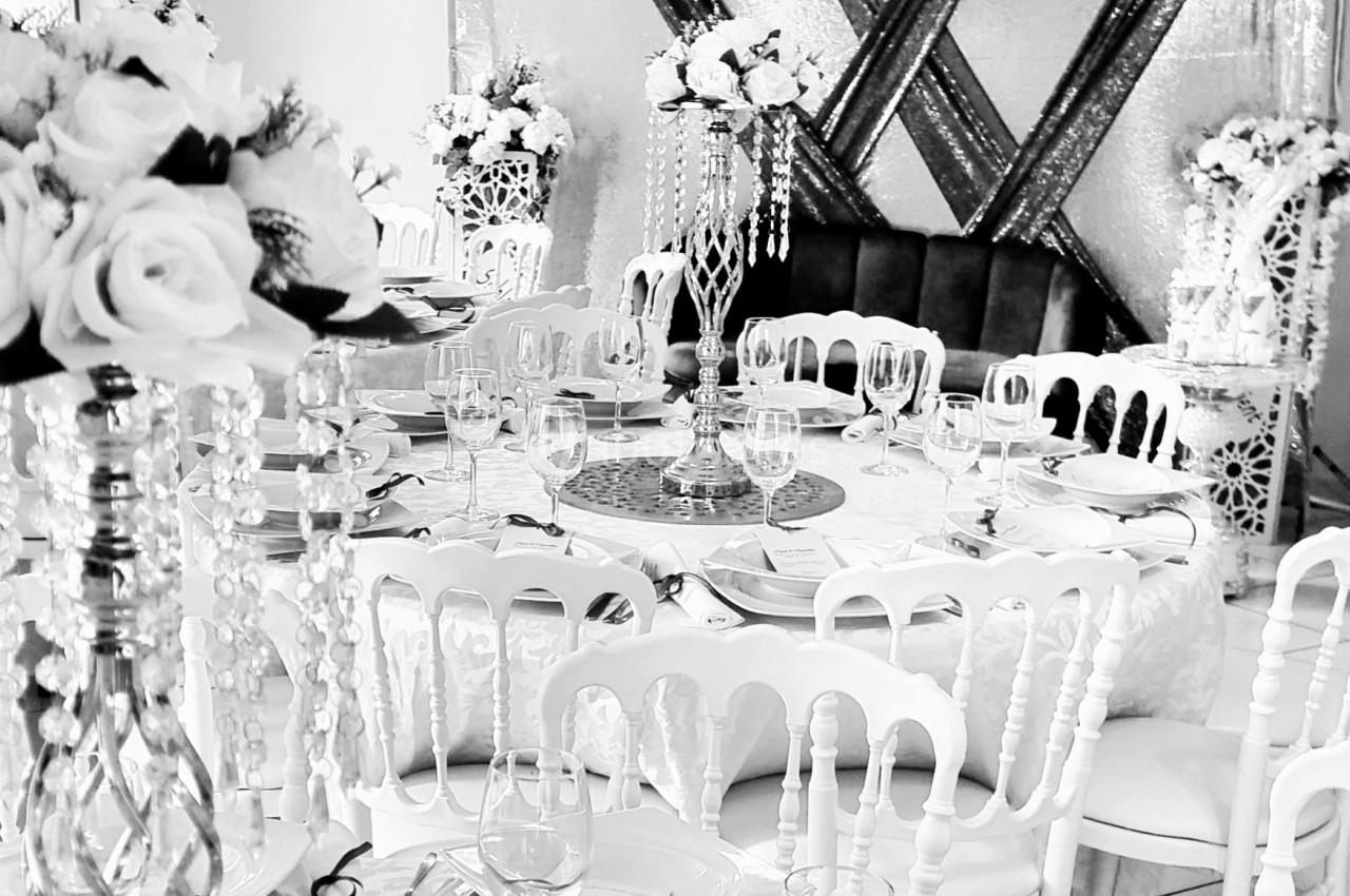 Salle de réception élégante avec tables décorées de nappes blanches, chandeliers ornés et compositions florales.