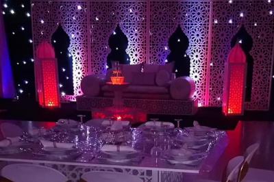 Salle de réception décorée avec des tables élégantes, nappes blanches, centres de table lumineux et plumes blanches.