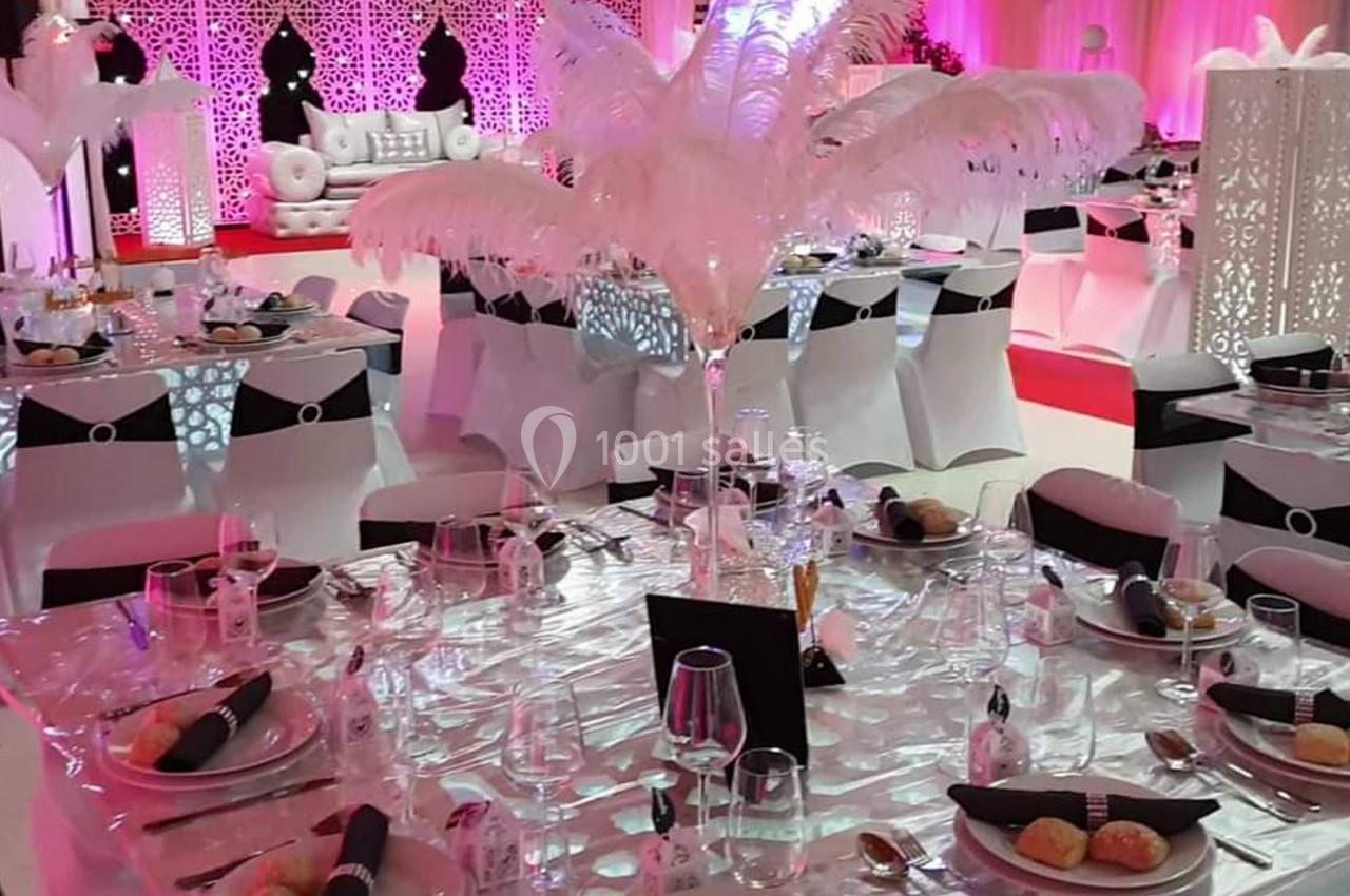 Salle de réception décorée avec des tables dressées, nappes blanches, plumes en centre de table et éclairage rose.