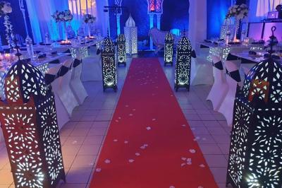 Salle de réception décorée avec des tables élégantes, nappes blanches, centres de table lumineux et plumes blanches.