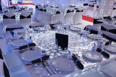 Salle de réception décorée avec des tables élégantes, nappes blanches, centres de table lumineux et plumes blanches.