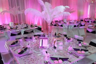Salle de réception décorée avec des tables élégantes, nappes blanches, centres de table lumineux et plumes blanches.