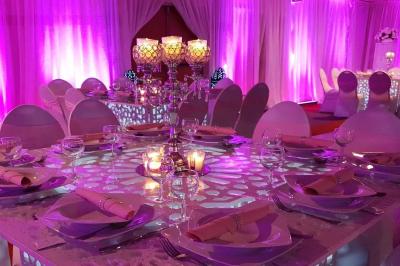 Salle de réception décorée avec des tables élégantes, nappes blanches, centres de table lumineux et plumes blanches.