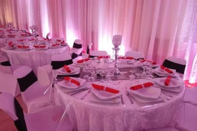 Salle de réception décorée avec des tables élégantes, nappes blanches, centres de table lumineux et plumes blanches.