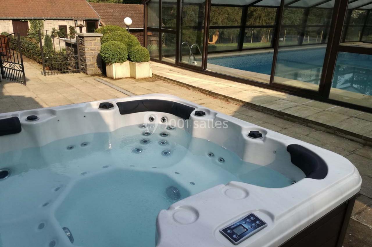 Spa extérieur avec jets massants au premier plan, près d'une piscine couverte entourée de verdure.