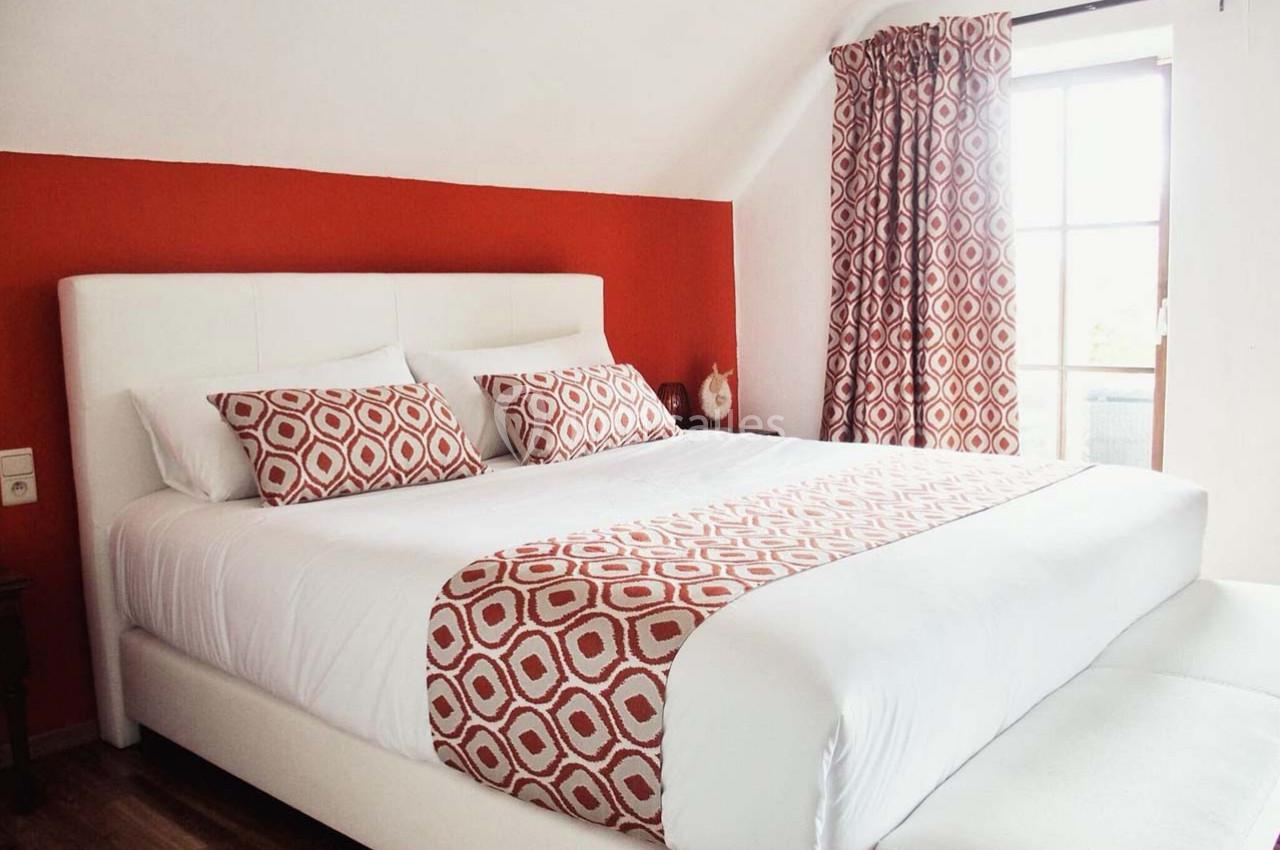 Lit double avec tête de lit blanche, draps et coussins à motifs géométriques rouges, dans une chambre lumineuse.