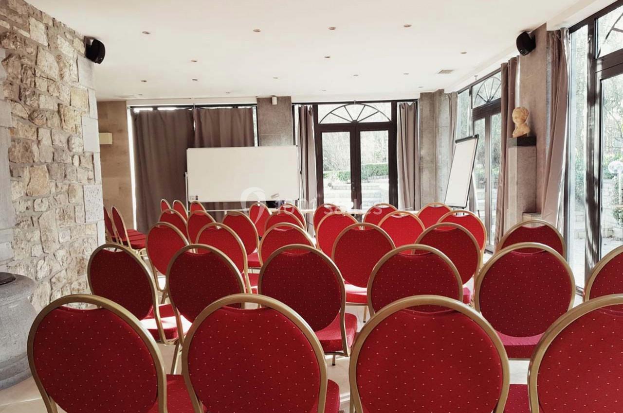 Salle de réunion lumineuse avec des chaises rouges alignées face à un tableau blanc et un chevalet.