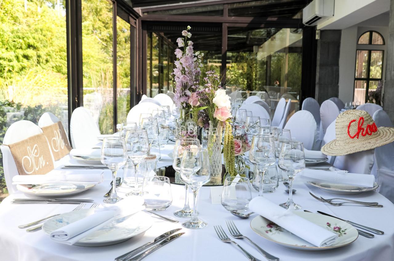 Table élégamment dressée pour un repas, avec vaisselle raffinée, fleurs en centre de table et chaises blanches.