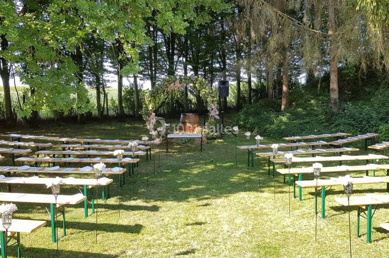 Disposition de bancs en bois et métal dans un espace extérieur verdoyant, avec une arche florale au centre.