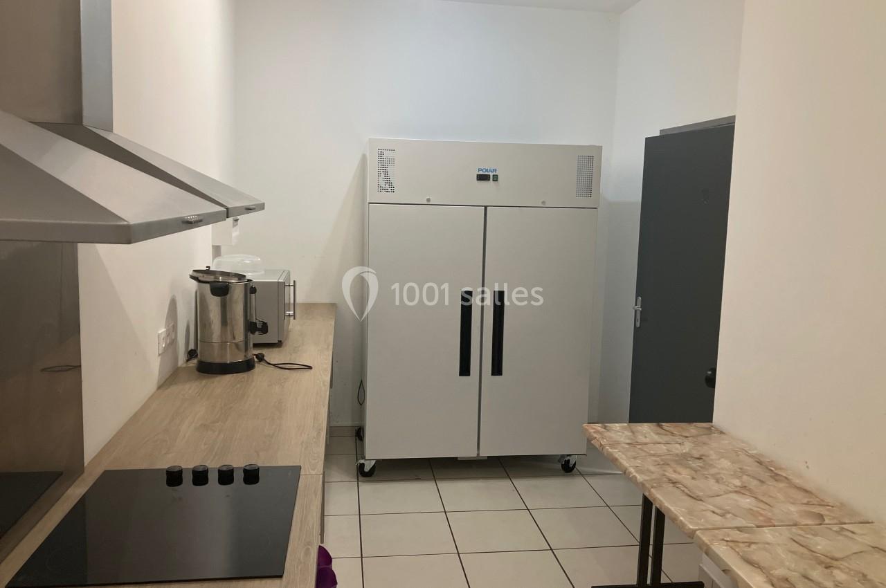 Cuisine équipée avec un plan de travail, plaques de cuisson, hotte, réfrigérateur professionnel et table en marbre.