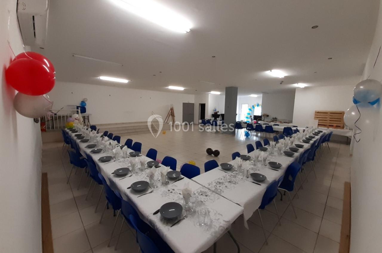 Salle de réception avec deux longues tables dressées en U, décorée de ballons et prête pour un événement.