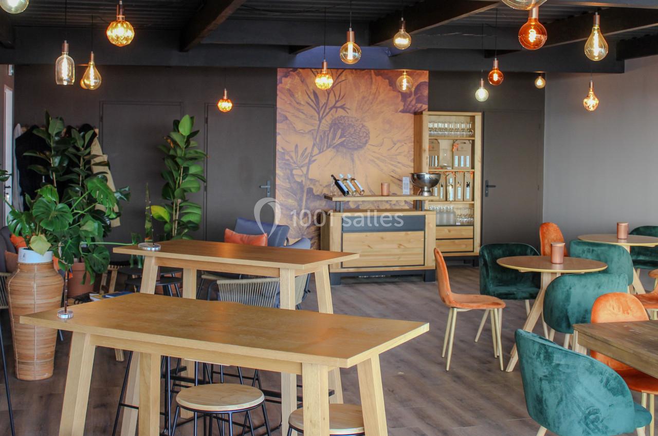 Salle lumineuse avec tables en bois, chaises colorées, plantes vertes et éclairage suspendu varié.