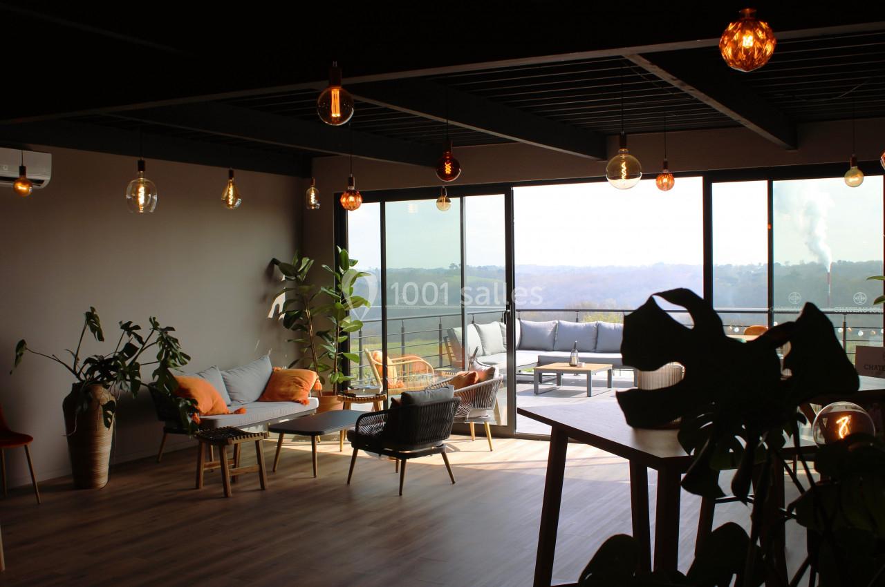 Espace lumineux avec mobilier moderne, plantes d'intérieur et grandes baies vitrées donnant sur une terrasse et un paysage.