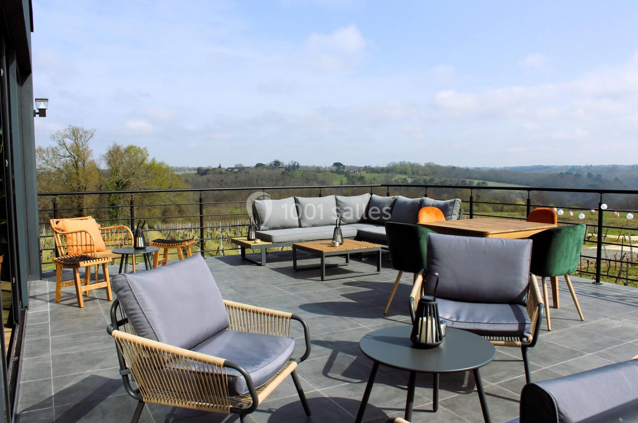 Terrasse spacieuse avec mobilier de jardin moderne, vue dégagée sur une campagne verdoyante sous un ciel partiellement…