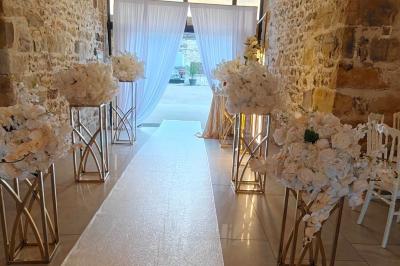 Allée décorée de fleurs blanches dans une salle en pierre éclairée par des guirlandes lumineuses.