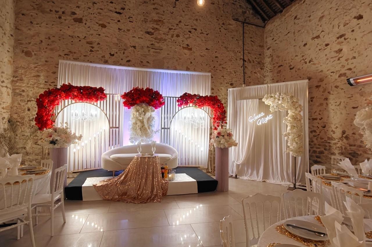 Salle décorée pour un événement avec un canapé blanc, des fleurs rouges et blanches, et une table ornée de doré.